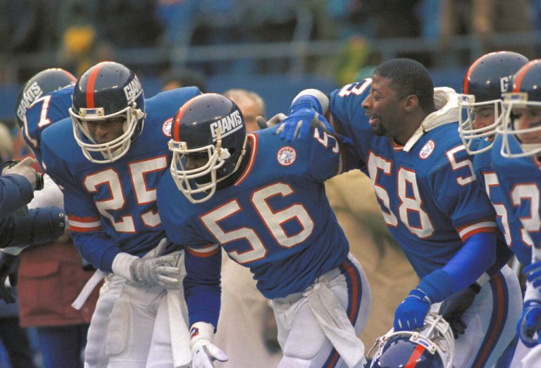 New York Giants linebacker Lawrence Taylor (56) is congregated by Mark Collins (25) and Carl Banks (58) after his interception and touchdown run on a Joe Montana pass in the second quarter on Sunday, Jan. 4, 1986 in East Rutherford, N.J. at Giants stadium. The interception helped the Giants beat the San Francisco 49 ers 49-3 in their NFL playoff game.